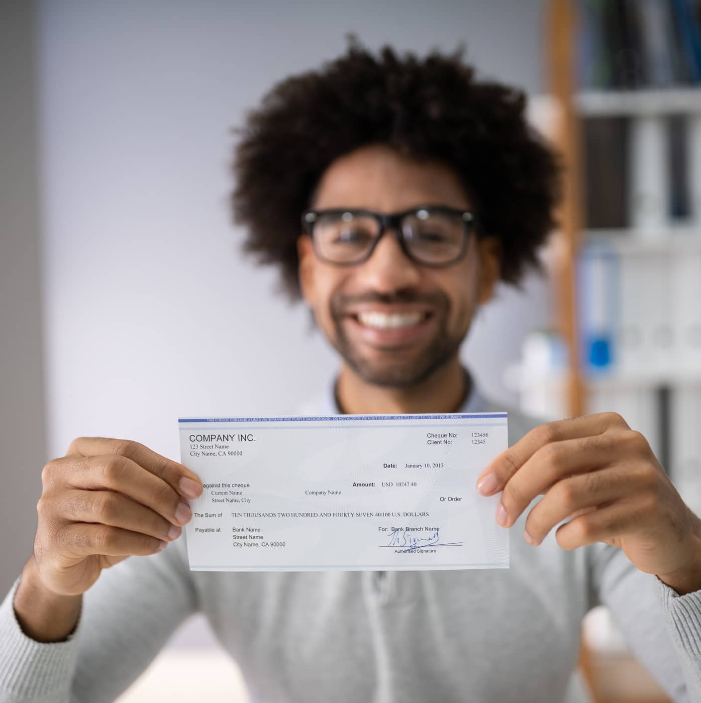 Person smiling and holding a paycheck while sitting indoors